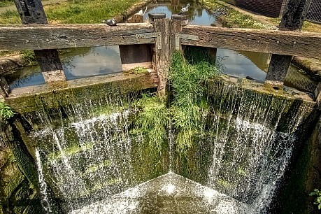 Water pouring down the inside of an old boat lock in sunshine.